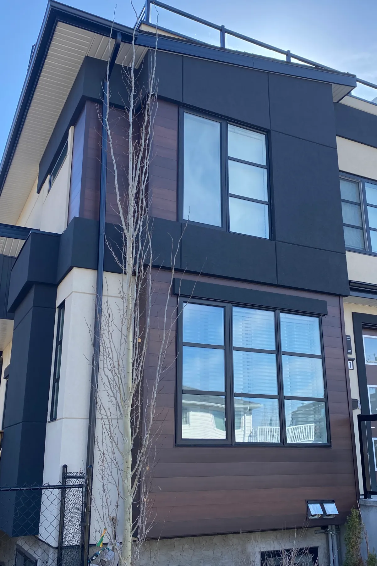 Exterior view of a two-story residential triplex featuring black and beige acrylic stucco with horizontal groove joints and wood siding accents.