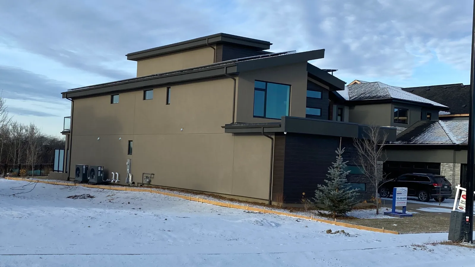 Modern two-story custom home in Edmonton with beige EIFS stucco and dark stone masonry during winter construction phase.