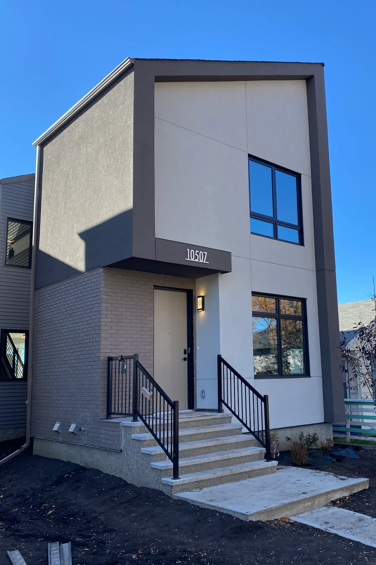 Side view of a residential building in Edmonton showing a brick veneer lower level transitioned into a dark grey acrylic stucco upper level.