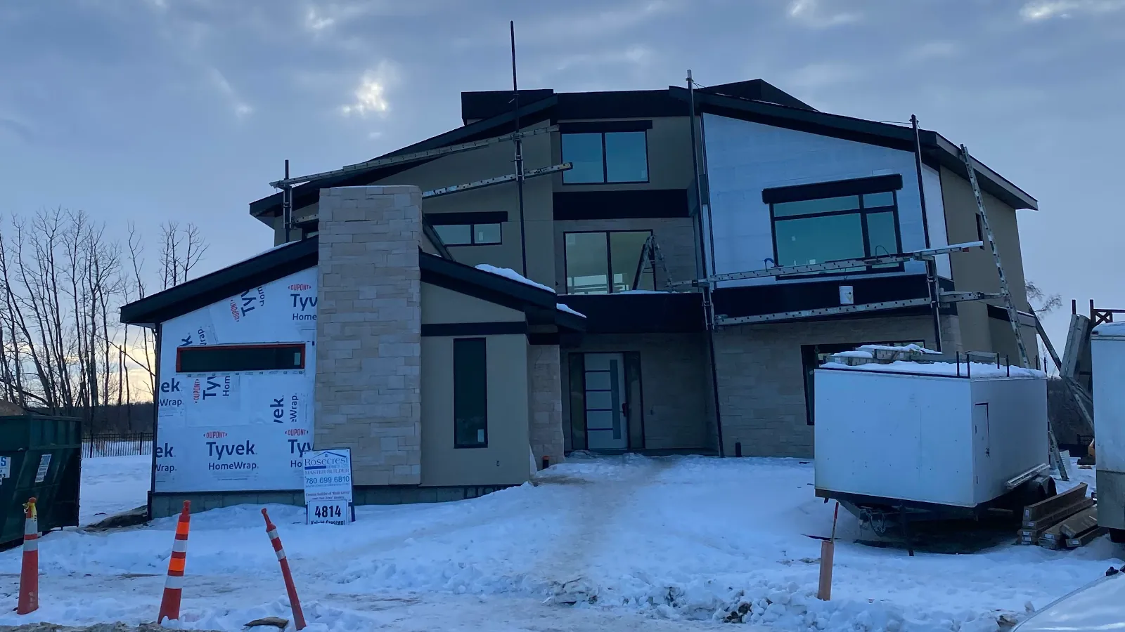 Front view of a three-story residence featuring light golden culture stone on a chimney and beige acrylic stucco finishes.