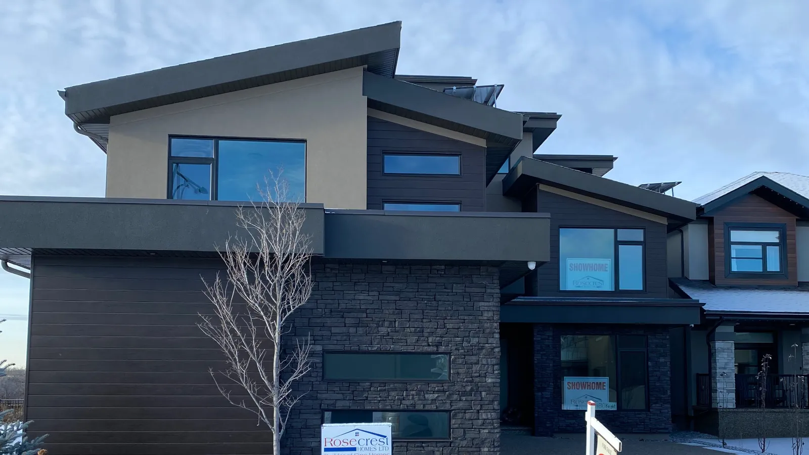 Front view of a two-story modern house in Edmonton featuring beige acrylic stucco, dark stacked culture stone, and a three-car garage.
