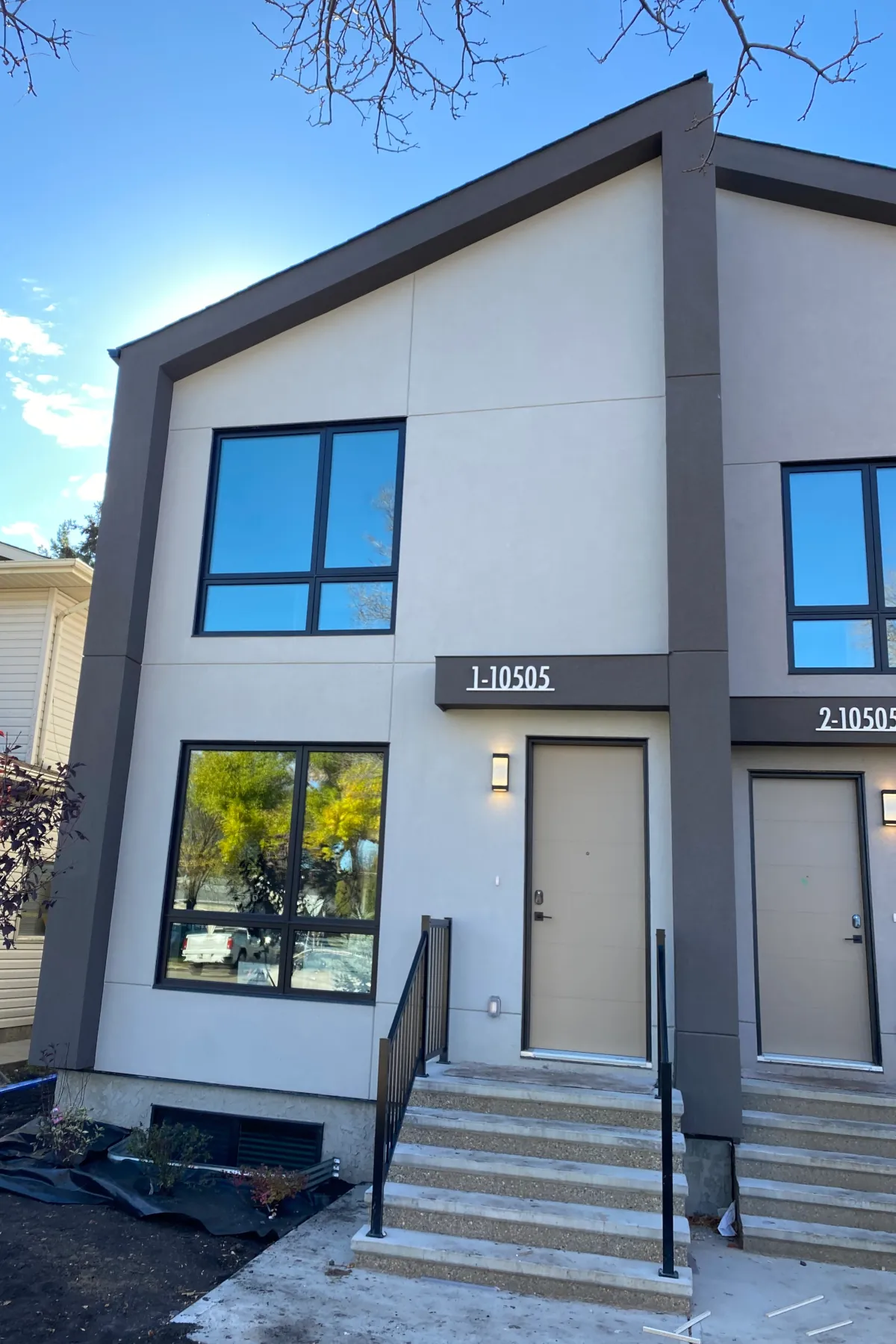 Front exterior of a modern two-story duplex in Edmonton featuring light beige acrylic stucco, dark grey borders, and horizontal aesthetic grooves.