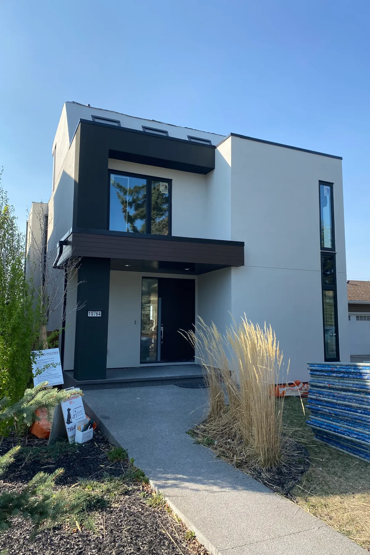 Front elevation of a two-story infill house in Edmonton featuring beige and charcoal acrylic stucco and a dark wood-textured porch header.