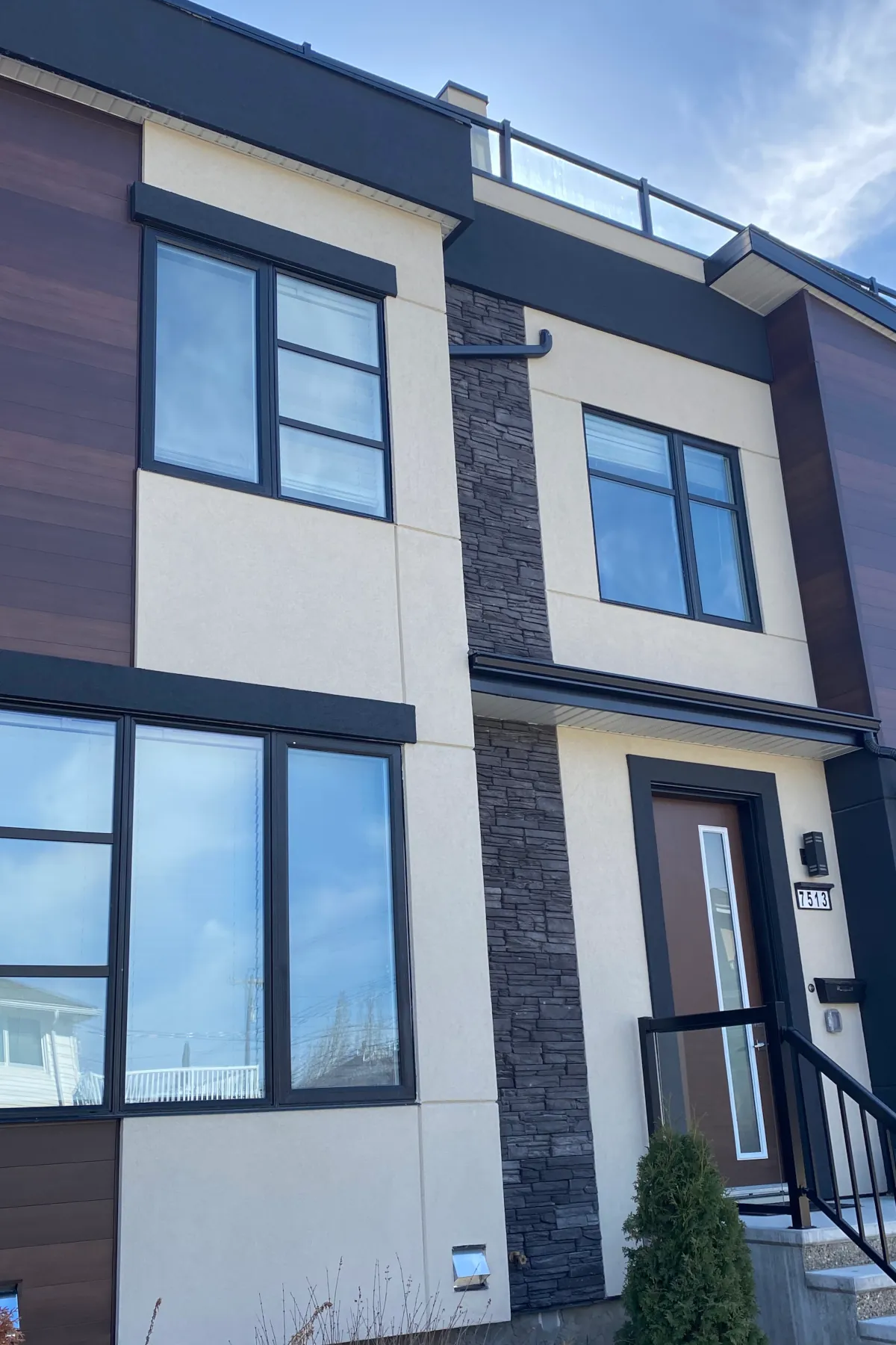 Front elevation showing the intersection of wood-textured siding, beige stucco, and black charcoal culture stone.