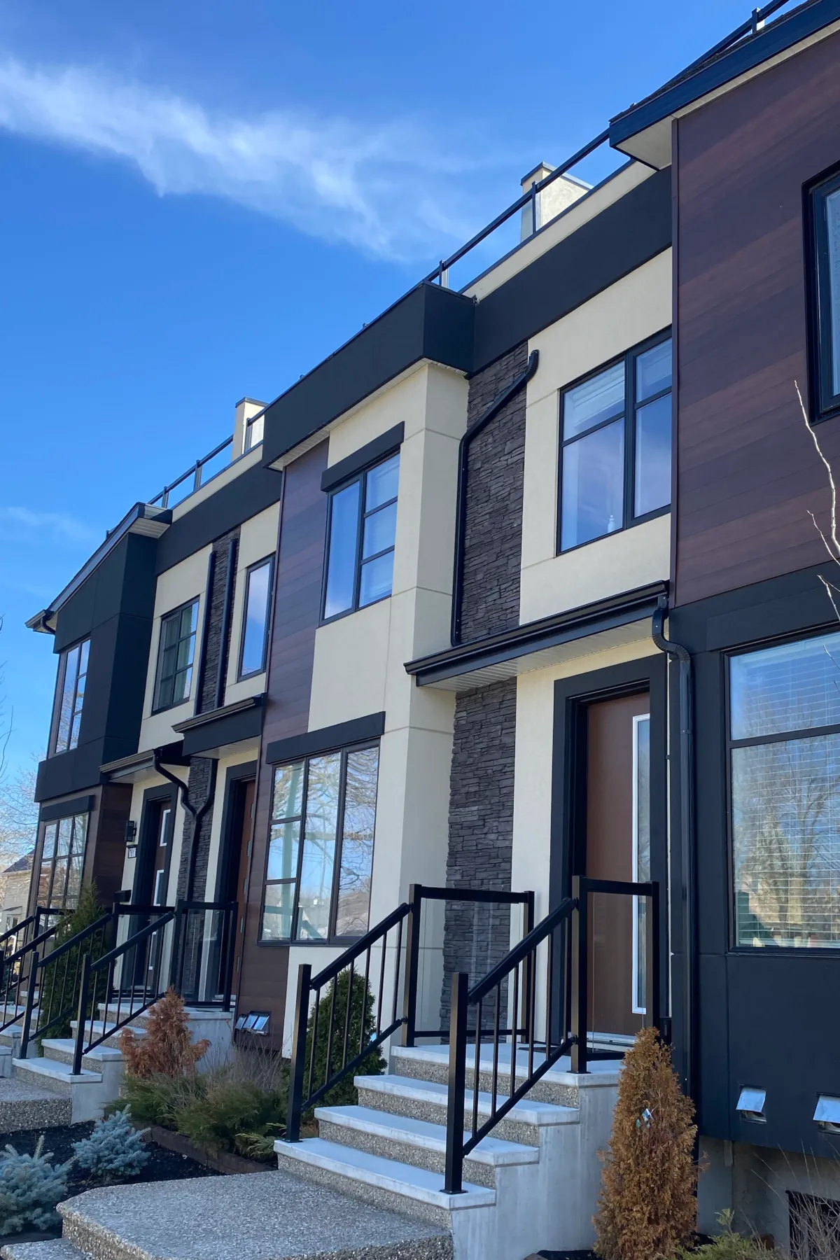 Wide-angle view of a modern triplex showcasing the complete exterior finish including stucco, stone, and rooftop glass railings.