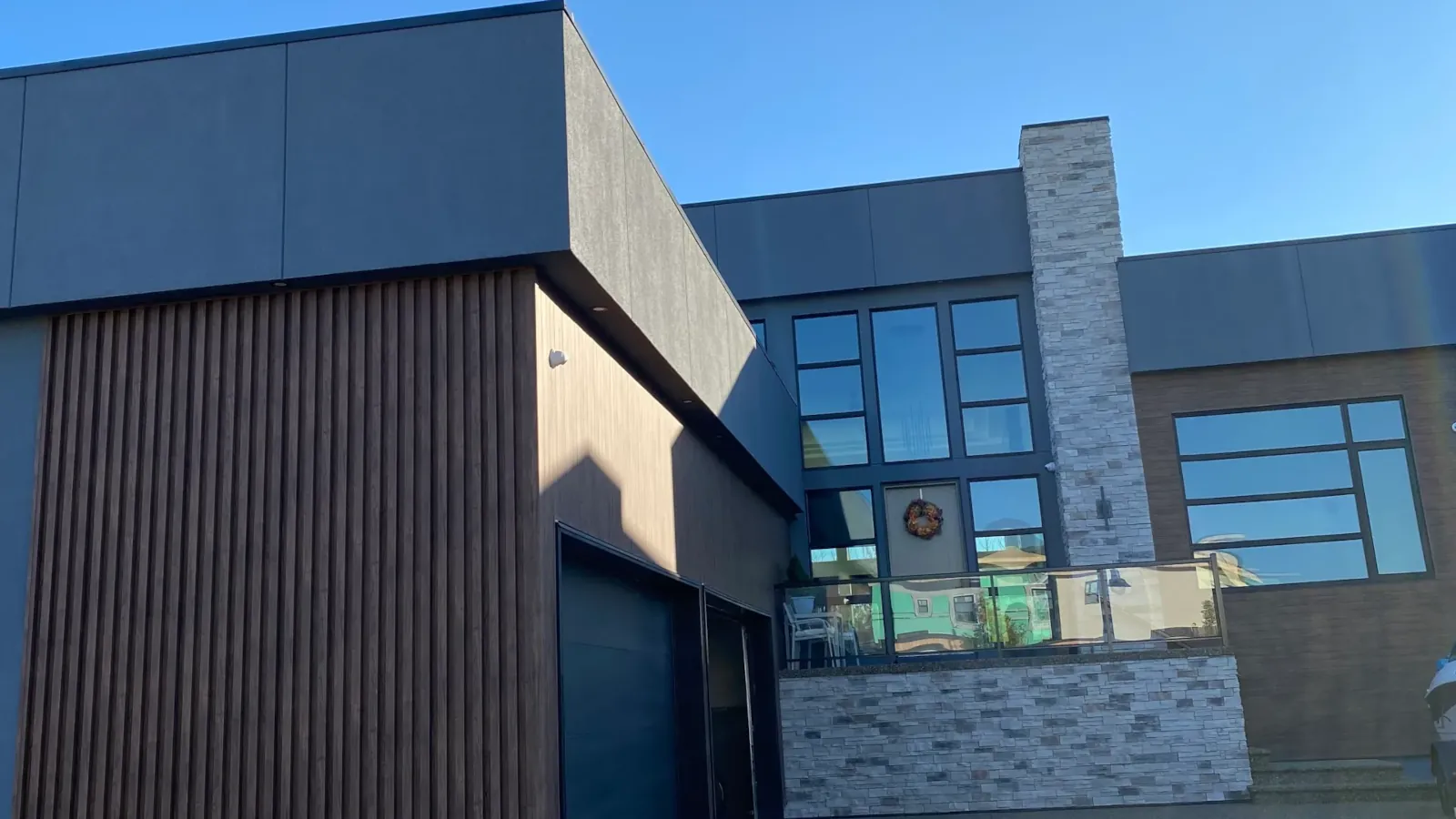 Architectural dark grey stucco finish on a luxury home with stone and wood accents in Devon near Edmonton, installed by AxisLayer Exteriors.